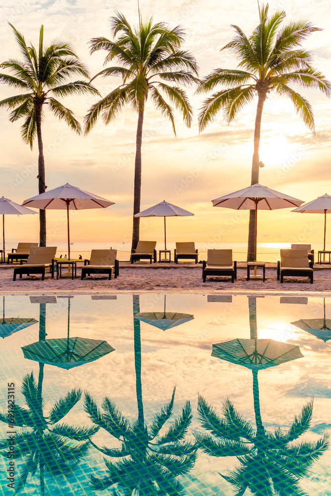 Sunrise over a tropical beach with palm trees, sun loungers, and umbrellas reflected in a pool's still water creates an inviting scene perfect for a luxury family travel agent to share with clients seeking the ultimate getaway.